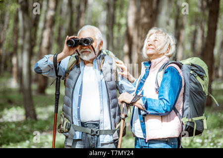 Coppia senior guardando con il binocolo durante le escursioni nella foresta. Concetto di uno stile di vita attivo su pensionamento Foto Stock