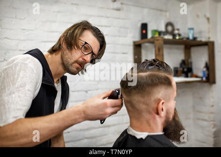 Elegante barbiere tagli brutali di un uomo con una folta barba. Foto Stock