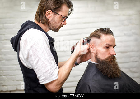 Elegante barbiere tagli brutali di un uomo con una folta barba. Foto Stock