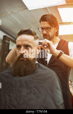 Elegante barbiere tagli brutali di un uomo con una folta barba. Foto Stock