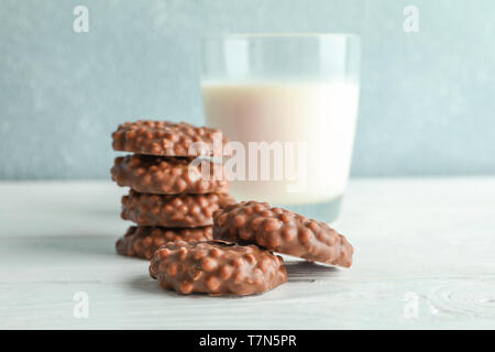 Pila di biscotti al cioccolato con bicchiere di latte sul tavolo bianco contro uno sfondo chiaro Foto Stock