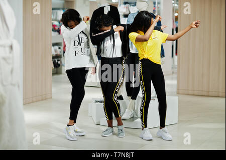 Afican tre donne americane in tute shopping al centro commerciale di abbigliamento sportivo contro il manichino. Lo sport store tema. Mostra DAB. Foto Stock