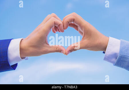 Amore il concetto di simbolo. Le mani di mettere assieme in forma di cuore cielo blu sullo sfondo. Mani maschio a forma di cuore simbolo del gesto di amore e romanticismo. Lato cuore gesto forme forma utilizzando le dita. Foto Stock