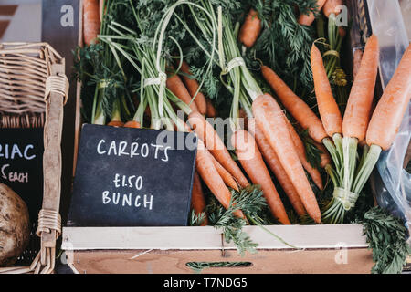 Close up di grappoli di materie organiche su carote in vendita in una cassa di legno, nero prezzo rustico tag nella cassa. Foto Stock