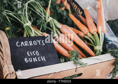 Close up di grappoli di materie organiche su carote in vendita in una cassa di legno, nero prezzo rustico tag nella cassa. Foto Stock