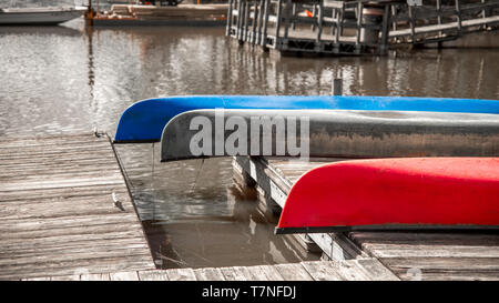 Tre canoe colorate appoggiato capovolto su un dock in legno con banchine in background Foto Stock