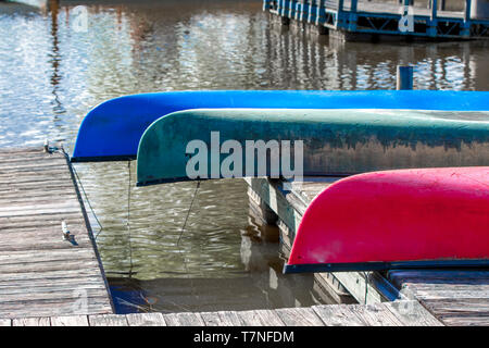 Tre canoe colorate appoggiato capovolto su un dock in legno con banchine in background Foto Stock