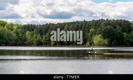 Uomo in camicia verde in piedi sul dock con due secchi e le foreste in background Foto Stock