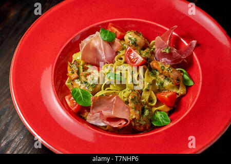 Pasta con gamberi e pancetta, decorato con foglie di basilico e i pomodori su una targhetta rossa. Legno scuro dello sfondo. Il menu del ristorante Foto Stock