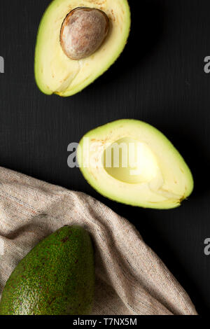 Intero e dimezzato avocadi oltre la superficie nera, vista dall'alto. Da sopra, overhead, piatto laici. Foto Stock
