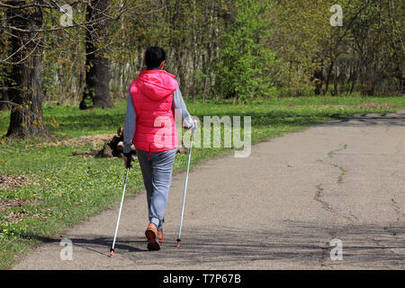 Nordic walking, la terapia per la salute. Giovane donna camminare con bastoni in primavera park, sport esercizi per la colonna vertebrale sana e giunti Foto Stock