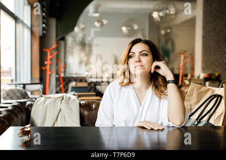 Giovane bella donna si siede in intimo cafe, guarda fuori della finestra Foto Stock