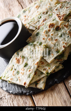 Vegan lo scalogno frittelle sono un croccante di pan-cinesi fritti flatbread close-up su una scheda sul piano verticale. Foto Stock