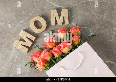Borsa regalo con bouquet di rose arancio e iscrizione Mom su sfondo marrone, vista dall'alto Foto Stock