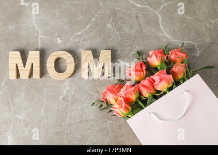 Borsa regalo con bouquet di rose arancio e iscrizione Mom su sfondo marrone, vista dall'alto Foto Stock
