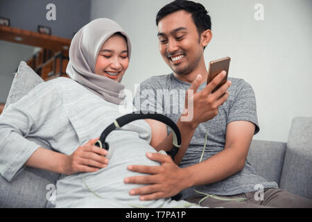 Donna incinta con cuffia sul suo ventre Foto Stock