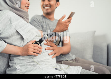 Donna incinta con cuffia sul suo ventre Foto Stock