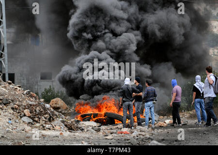 Giovani manifestanti e bruciando pneumatici durante la manifestazione di protesta contro gli insediamenti illegali e la confisca del villaggio di terre. Palestina Foto Stock