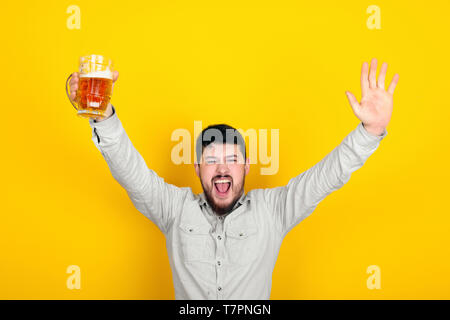 Gioioso uomo barbuto con un bicchiere di birra in mano su sfondo giallo Foto Stock