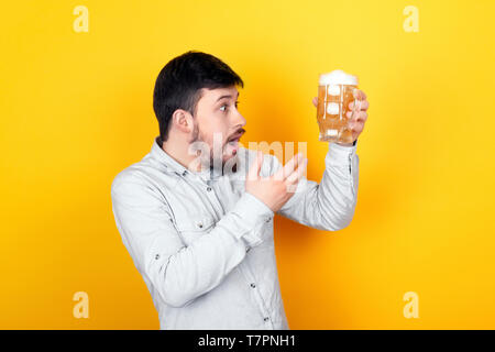 Ritratto in studio di un uomo sorpreso che è indignato per la qualità della birra, su sfondo giallo Foto Stock