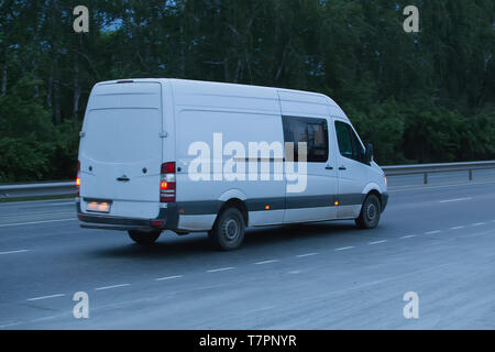 Piccolo bus bianco va in autostrada in sera Foto Stock