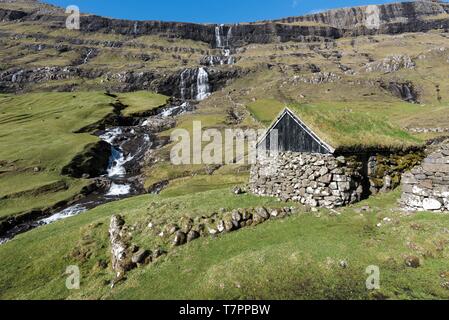 Danimarca, Isole Faerøer, Streymoy Isola, Saksun, tradizionale casa in pietra con il tetto del fondo erboso e cascata in background Foto Stock