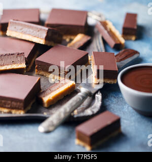 Cioccolato fette di caramello, barre, milionari frollini su un vassoio di metallo Sfondo blu. Close up. Foto Stock