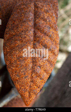 Close up di un pezzo di metallo sagomata come una foglia, marrone e arancione, su sfondo di messa a fuoco Foto Stock