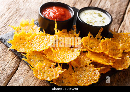 Delizioso croccante di formaggio cheddar chip con erbe aromatiche con salse close-up su una scheda su una tavola orizzontale. Foto Stock