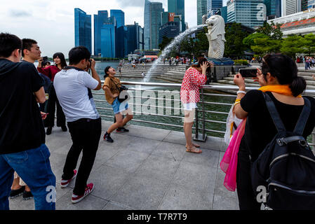 I turisti che posano per una foto davanti alla statua Merlion e dello skyline di Singapore, Singapore, Sud-est asiatico Foto Stock