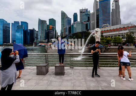 I turisti che posano per una foto davanti alla statua Merlion e dello skyline di Singapore, Singapore, Sud-est asiatico Foto Stock
