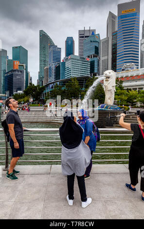 I turisti che posano per una foto davanti alla statua Merlion e dello skyline di Singapore, Singapore, Sud-est asiatico Foto Stock