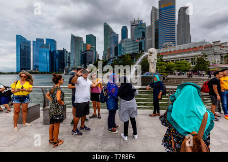 I turisti che posano per una foto davanti alla statua Merlion e dello skyline di Singapore, Singapore, Sud-est asiatico Foto Stock