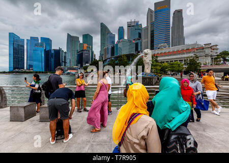 I turisti che posano per una foto davanti alla statua Merlion e dello skyline di Singapore, Singapore, Sud-est asiatico Foto Stock