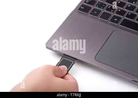 Vista ravvicinata di donna con la mano nera della scheda SD. Si collega a un lettore in argento di un portatile con una tastiera. Isolato su sfondo bianco. Foto Stock