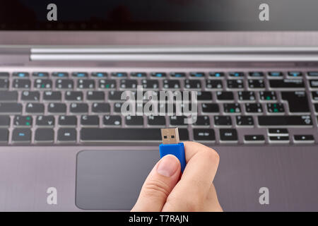 Vista ravvicinata di una donna a mano blu con supporto di memoria flash USB o un disco. Soft focus notebook color argento con tastiera sullo sfondo Foto Stock
