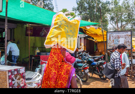 Scena di strada in Shahpura, un quartiere Dindori città nel Madhya Pradesh, India centrale: una donna locale che porta una borsa da shopping sul suo capo Foto Stock