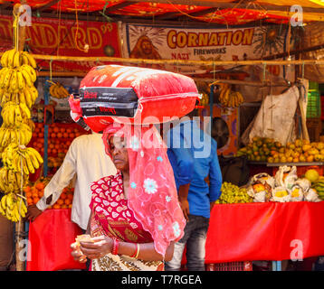 Scena di strada in Shahpura, un quartiere Dindori città nel Madhya Pradesh, India centrale: un vecchio locale donna contano i soldi che trasportano un pacchetto sul suo capo Foto Stock