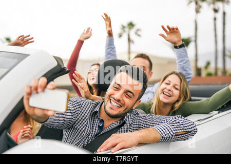 Happy amici prendendo selfie e la registrazione con mobile smart phone in autovettura convertibile - i giovani al divertimento in cabriolet auto durante il loro viaggio Foto Stock