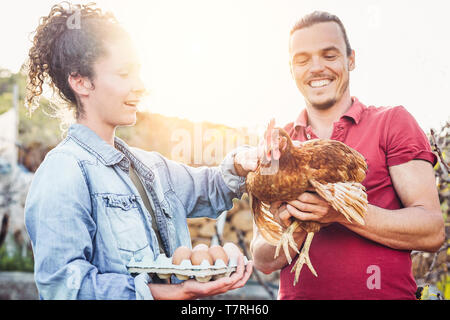 Coppia felice di agricultrist prelievo di uova fresche nel pollaio fattoria al tramonto - i giovani agricoltori che lavorano in fabbrica house Foto Stock