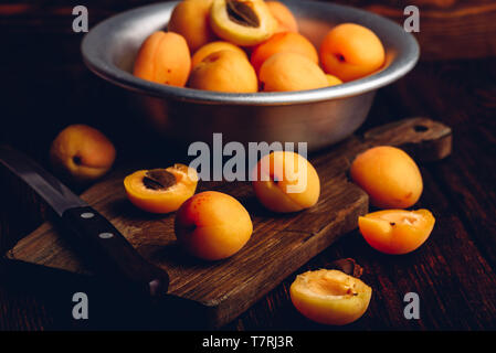 Mellow albicocche con il coltello su un vecchio tagliere di legno e metallo ciotola con frutti Foto Stock