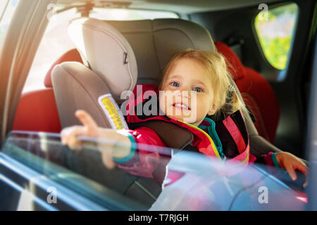 Poco sorridente ragazza seduta in un seggiolino da bambino per auto Foto Stock