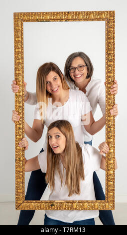 Famiglia composta da madre e due gemelle pongono all'interno di una cornice pittorica in uno studio fotografico e in un modo molto strano atteggiamento. Foto Stock