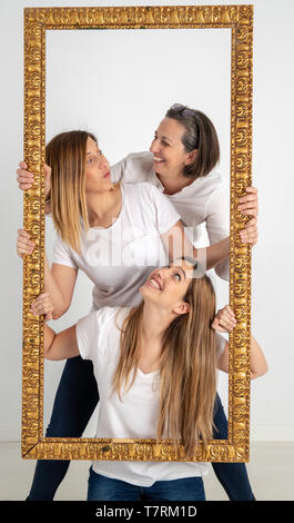 Famiglia composta da madre e due gemelle pongono all'interno di una cornice pittorica in uno studio fotografico e in un modo molto strano atteggiamento. Foto Stock