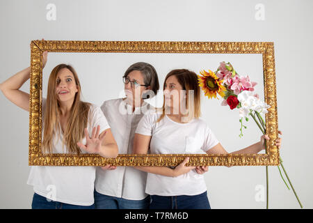 Famiglia composta da madre e due gemelle pongono all'interno di una cornice pittorica in uno studio fotografico e in un modo molto strano atteggiamento. Foto Stock