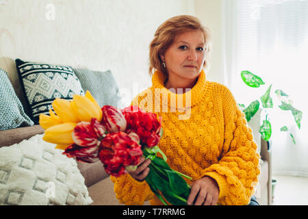 Senior donna holding bouquet di tulipani da i suoi bambini a casa. Giornata della madre presente Foto Stock