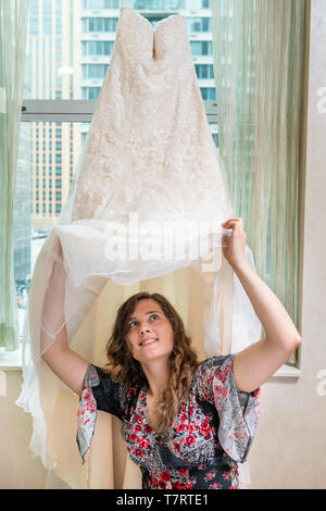 Donna giovane ragazza felice cercando su abito da sposa di finire sotto dal davanzale della finestra in ambiente urbano moderno hotel di città alta crescita appartamento condominio prima Foto Stock