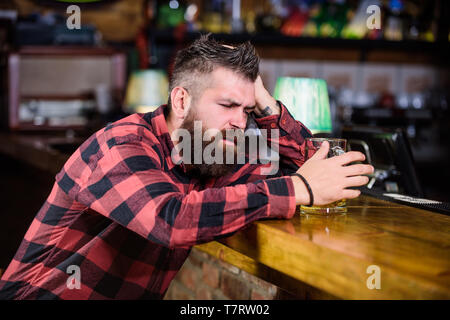 Il bar è un luogo rilassante hanno bere e rilassarsi. Uomo con barba trascorrere il tempo libero nella barra di colore scuro. Brutale parigamba uomo barbuto sedersi al banco bar bere birra. Hipster rilassante presso il bar con birra. Ordine di bere alcol. Foto Stock