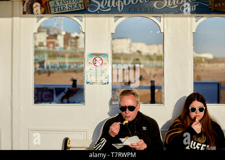 Tourist godendo di pesce e patatine sul molo di Brighton Foto Stock