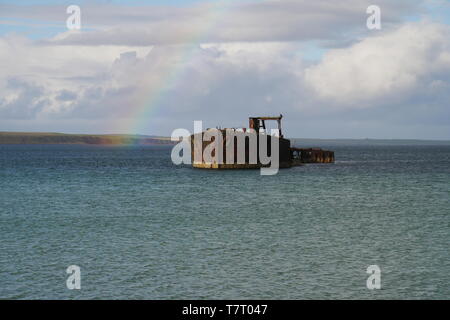 Il relitto della seconda guerra mondiale 2 ex blockship Juniata, nella baia di Inganess sulle isole Orcadi Scozia, Regno Unito, con un arcobaleno in background Foto Stock